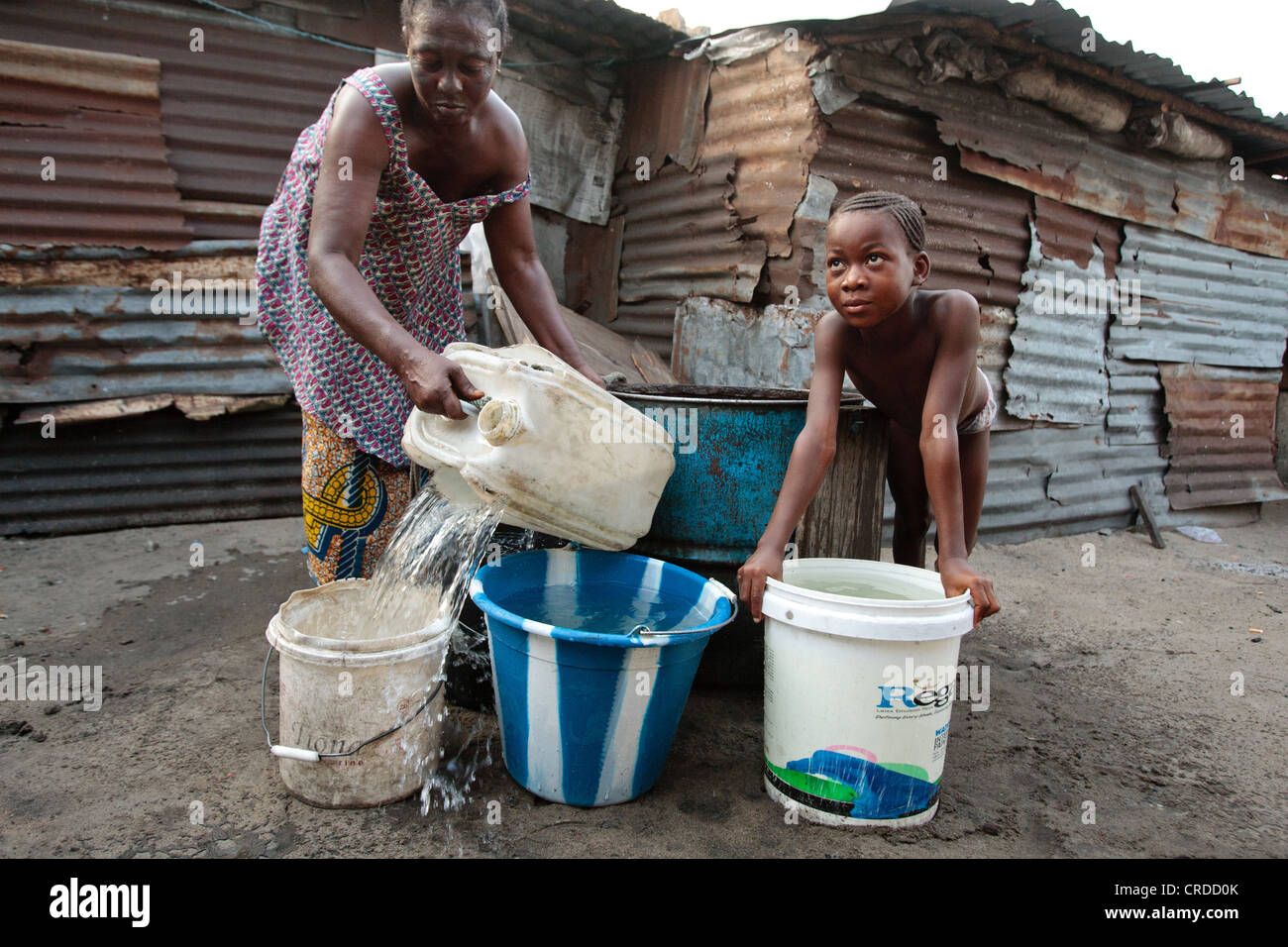 A girl watches while a woman draws water from a well in the West Point slum in Monrovia, Montserrado county, Liberia Stock Photo