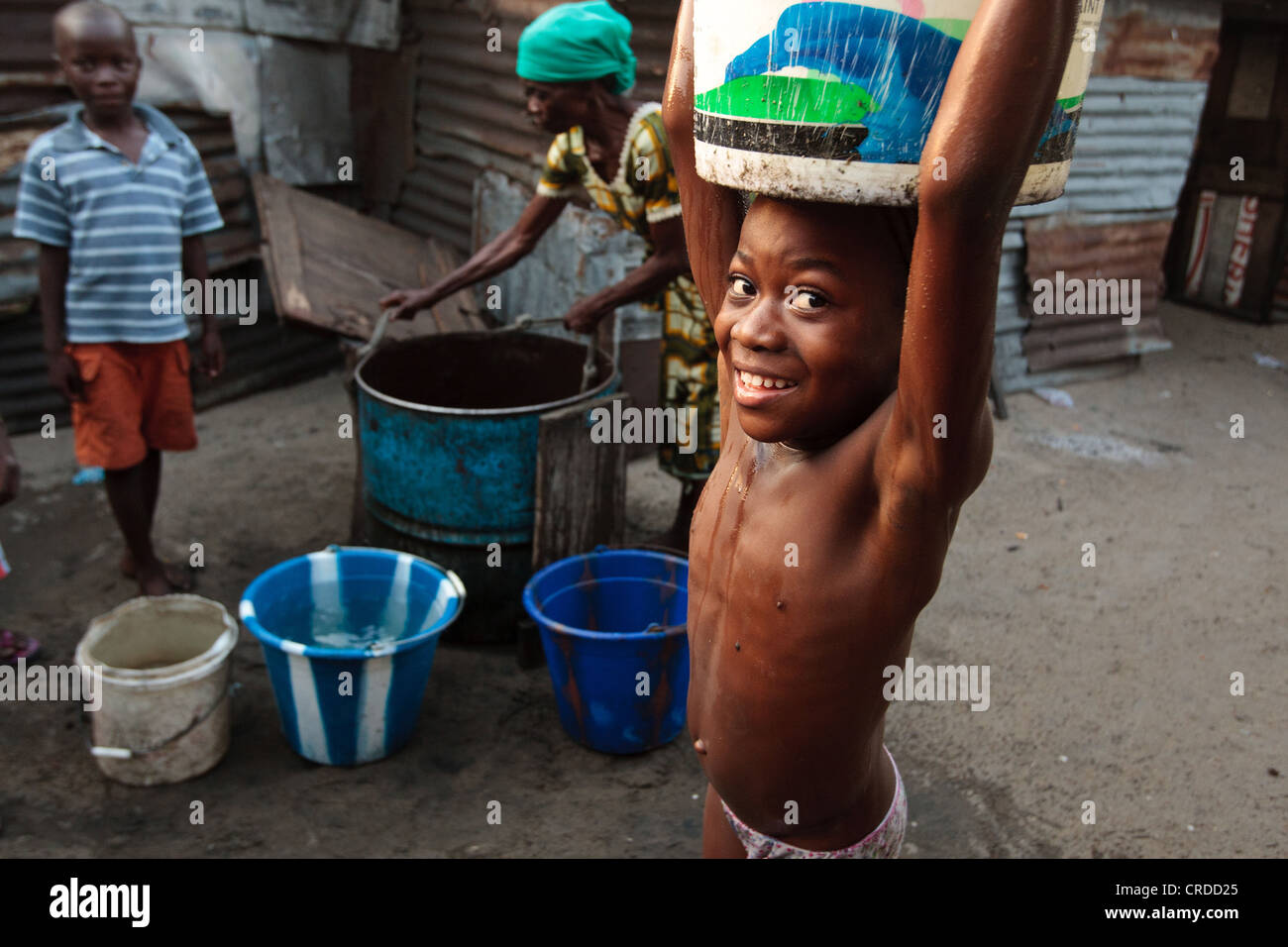 A girl carries a bucket of water she just filled from a well in the West Point slum in Monrovia, Montserrado county, Liberia Stock Photo
