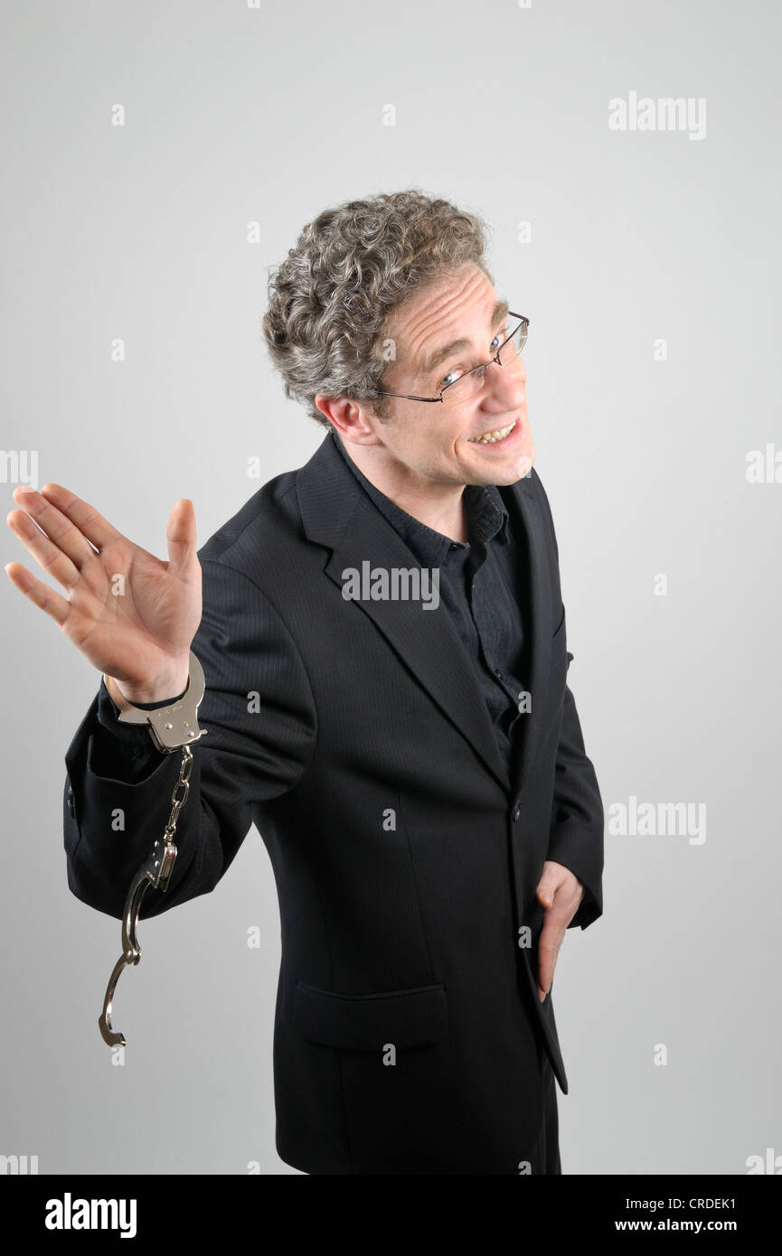 Businessman wearing a black suit and open handcuffs, waving and sneering Stock Photo