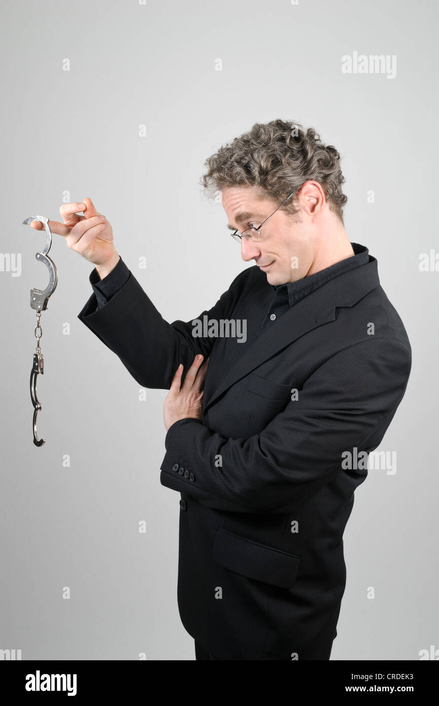 Businessman wearing a black suit looking at open handcuffs Stock Photo