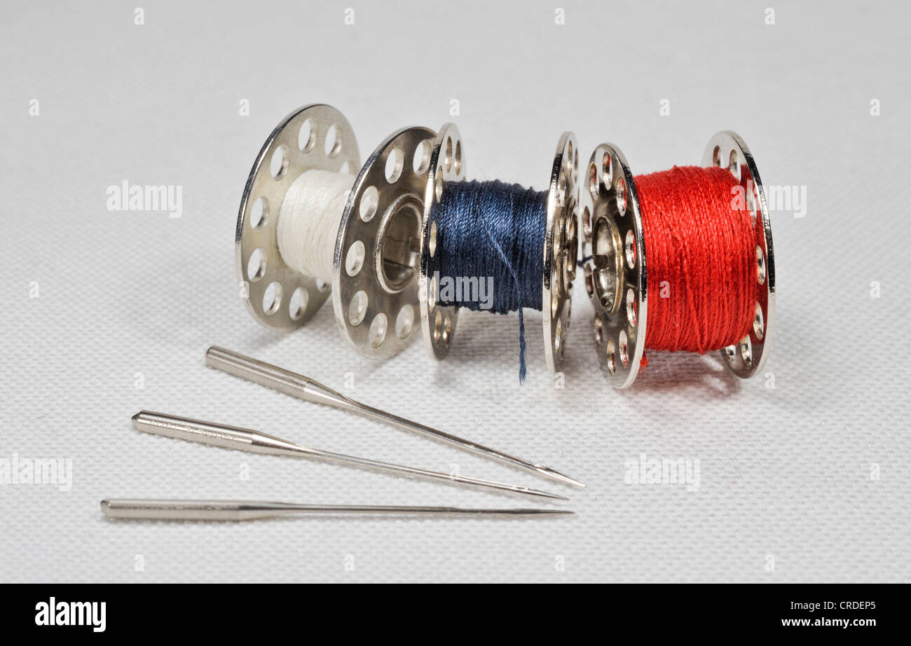 Sewing machine needles fanned out with yarn spools lying on white linen