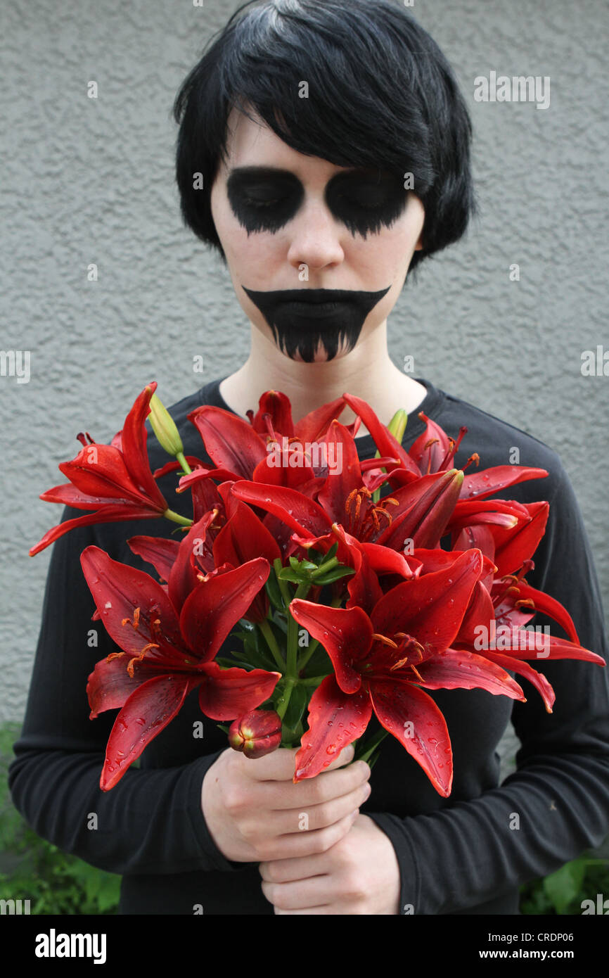A scary goth style girl holding a bouquet of red flowers Stock Photo