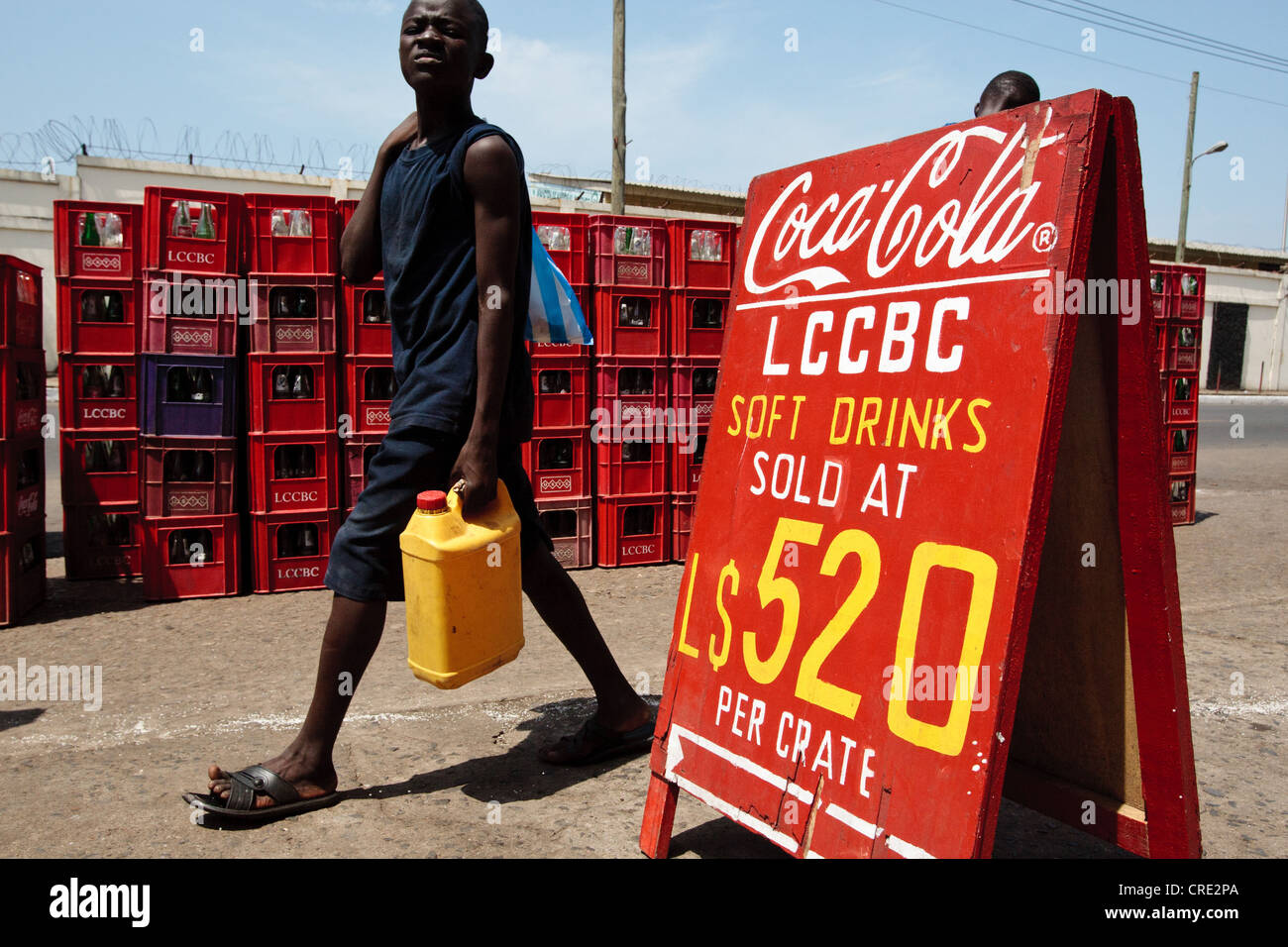 A boy walks past a sign advertising soft drinks for sale at Rally Time market in Monrovia, Montserrado county, Liberia Stock Photo