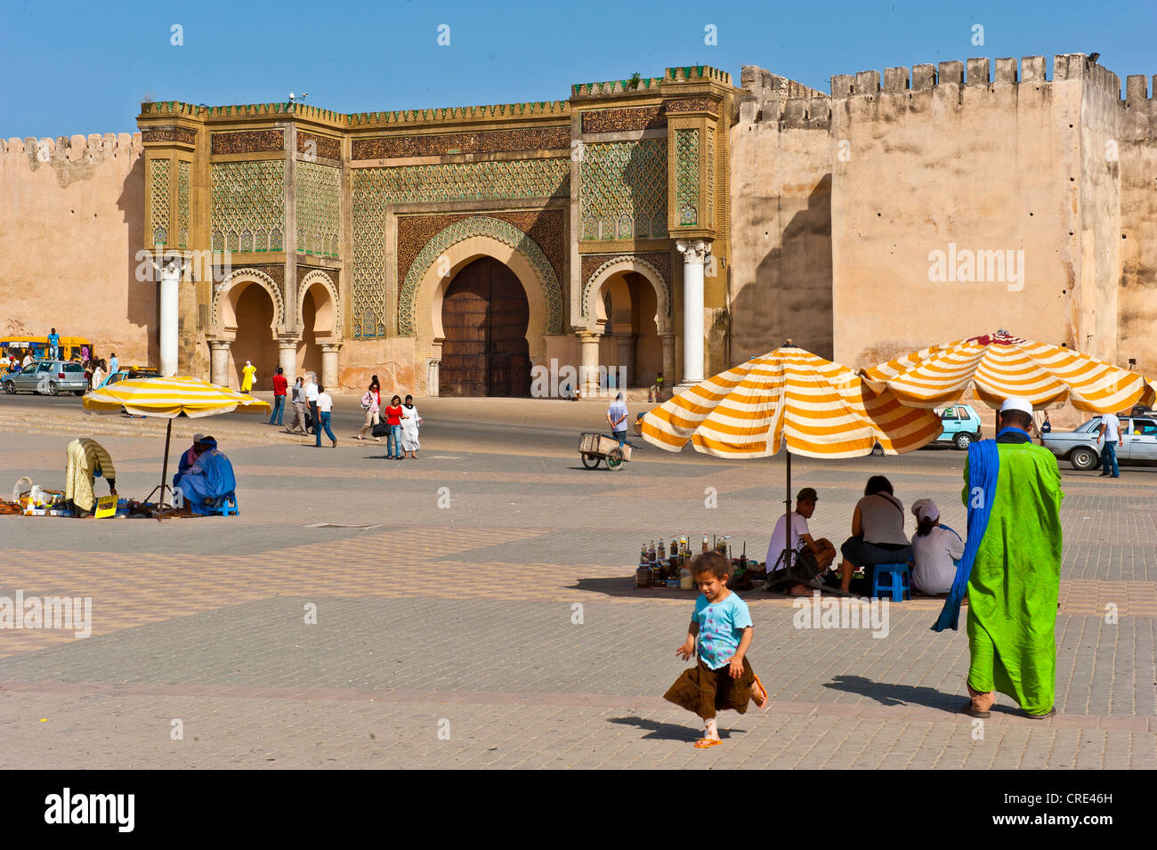 Old town gate, Bab Mansour, on the forecourt where vendors have spread out their wares for sale under umbrellas, Meknes, Morocco Stock Photo