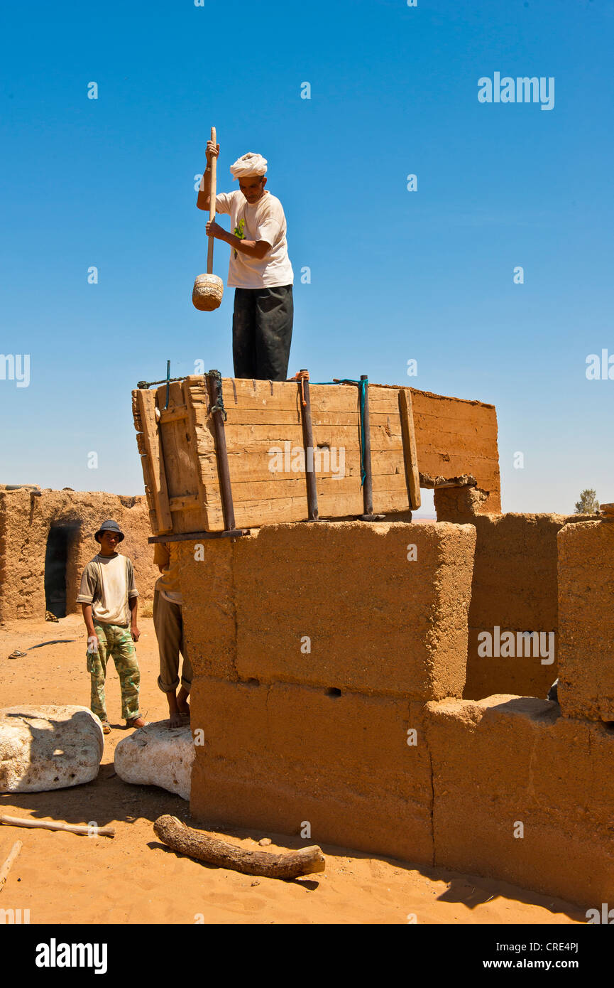 Elderly man wearing a white turban using a wooden tool to compact clay into a wooden casing for the construction of a wall made Stock Photo