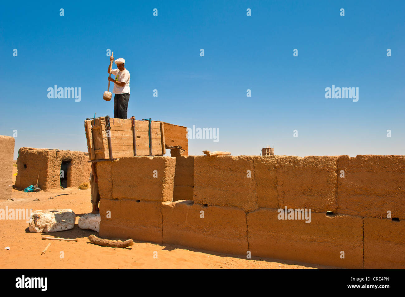 Elderly man wearing a white turban using a wooden tool to compact clay into a wooden casing for the construction of a wall made Stock Photo