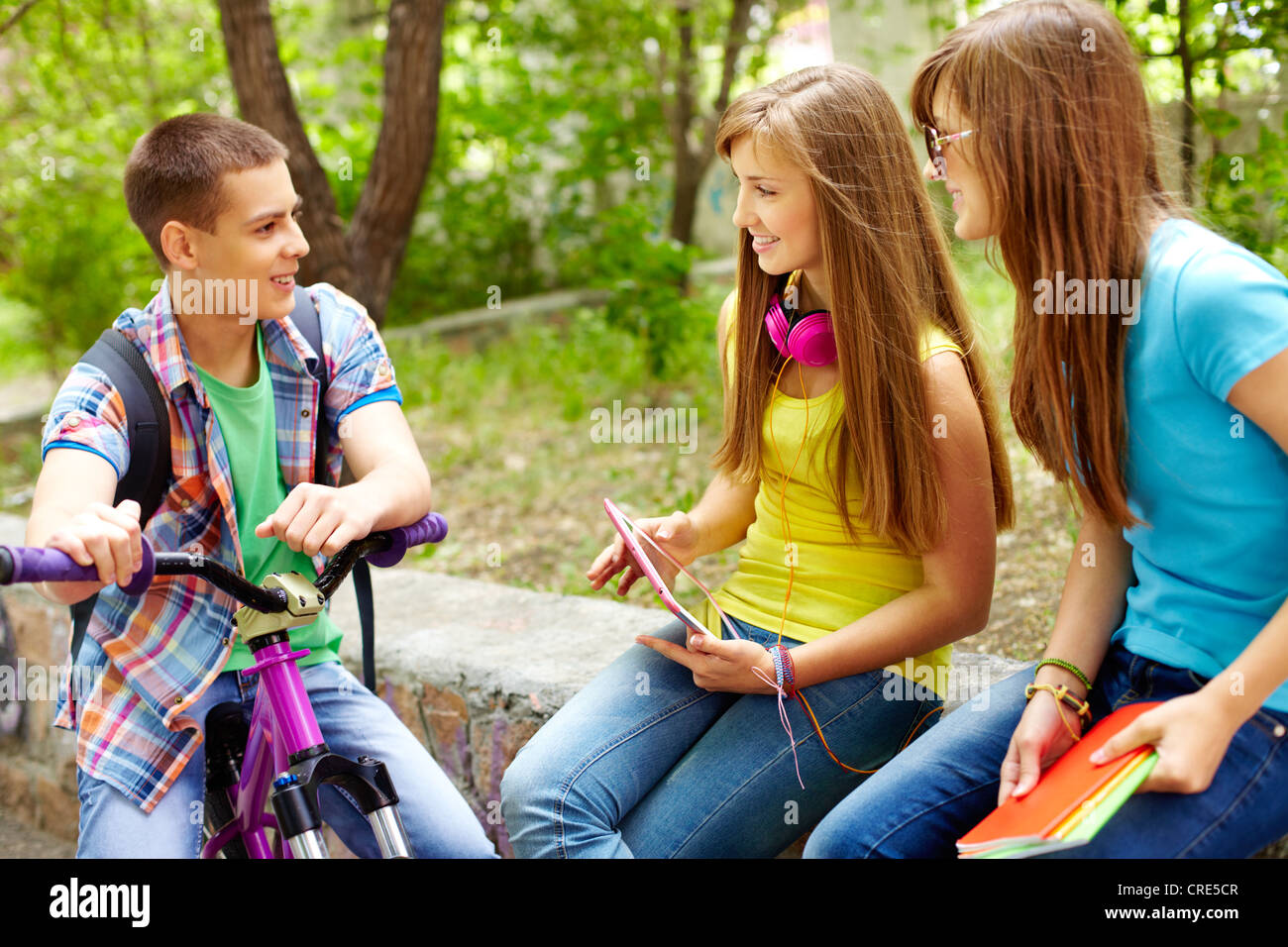 Bicycling boy meeting his female classmates in park Stock Photo