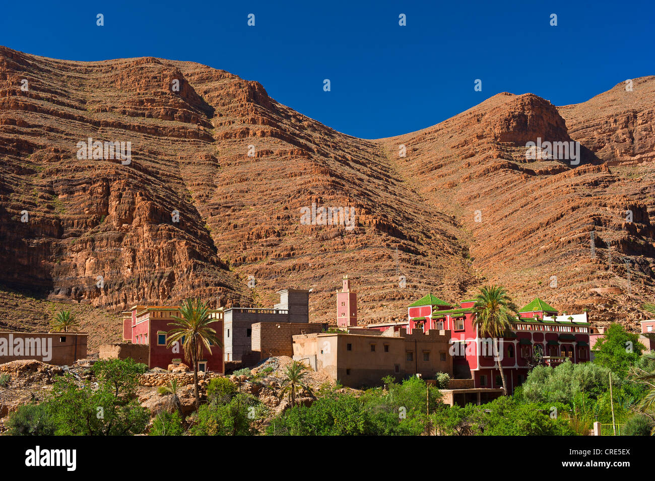 Small village with a mosque in front of red rock walls, Ait Mansour Valley, Anti-Atlas Mountains, southern Morocco, Morocco Stock Photo