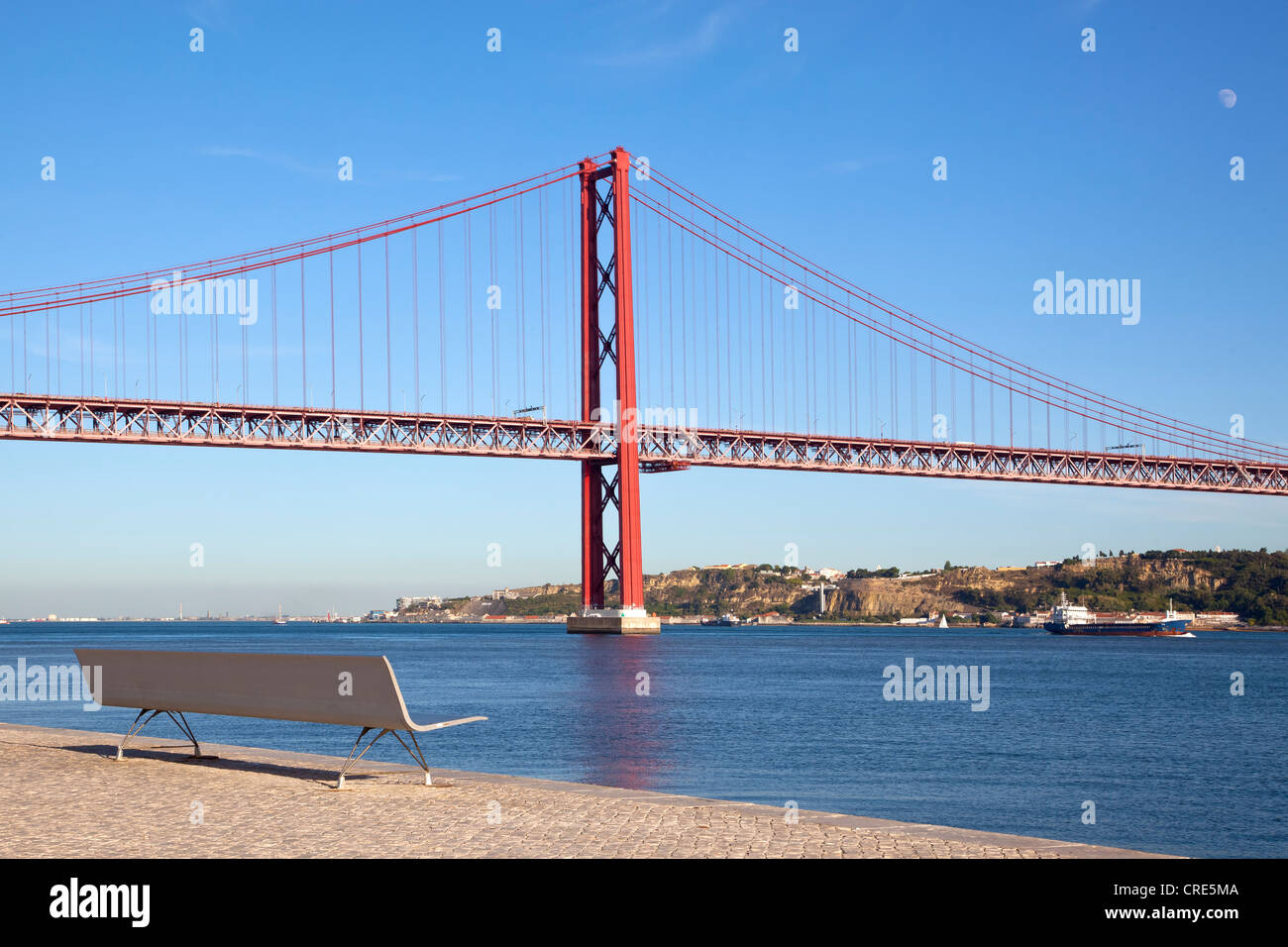 Bench on the bank of the Rio Tejo River in front of the Ponte do 25 de Abril bridge in the district of Belem, Lisbon, Portugal Stock Photo