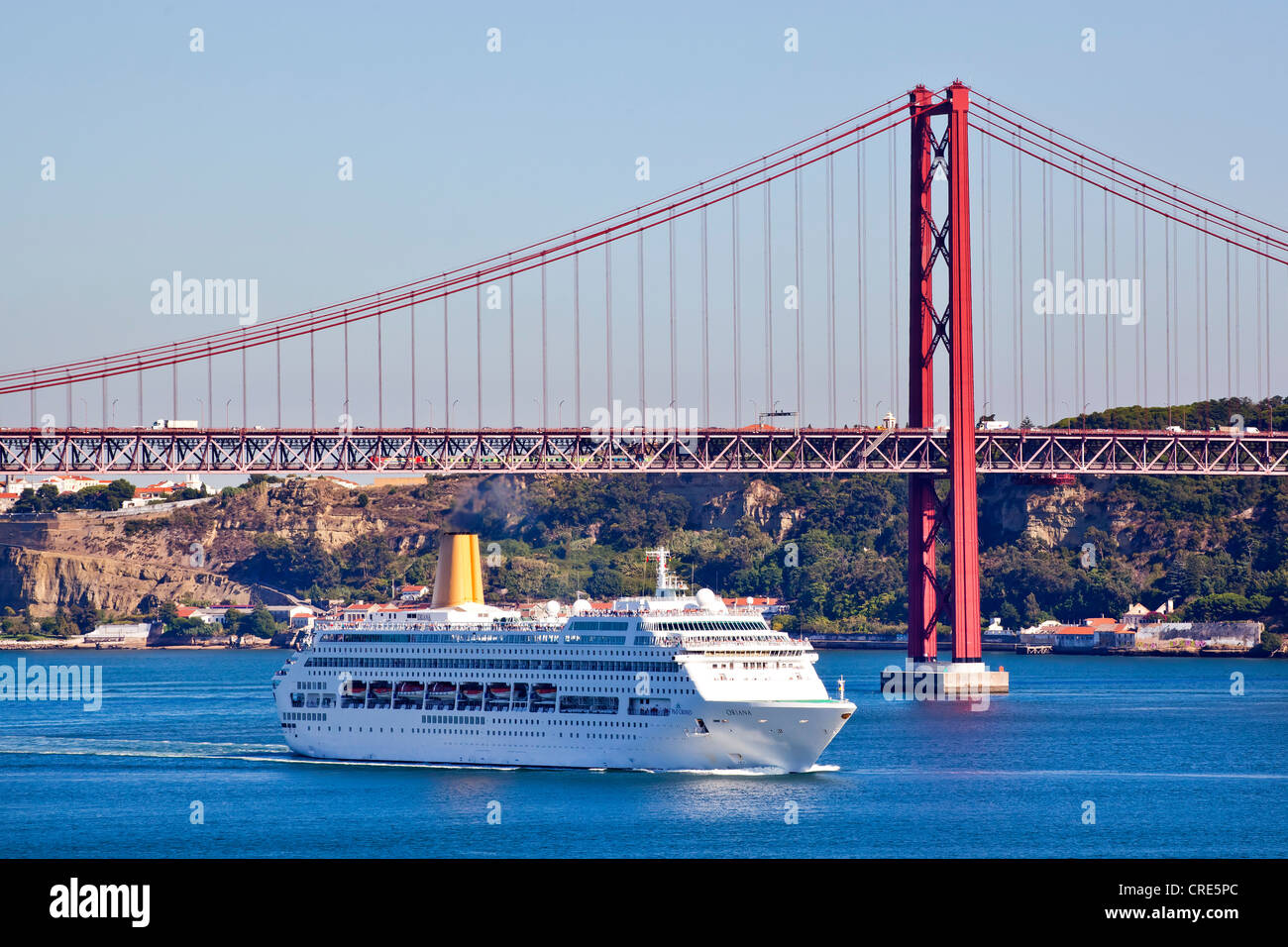 A cruise ship under the Ponte do 25 de Abril bridge, at the mouth of the Rio Tejo River in the Atlantic Ocean in the district of Stock Photo
