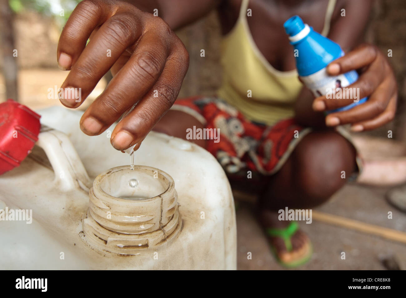 A woman uses a chlorine water treatment product to treat drinking water at home in the village of Kawejah, Grand Cape Mount Stock Photo