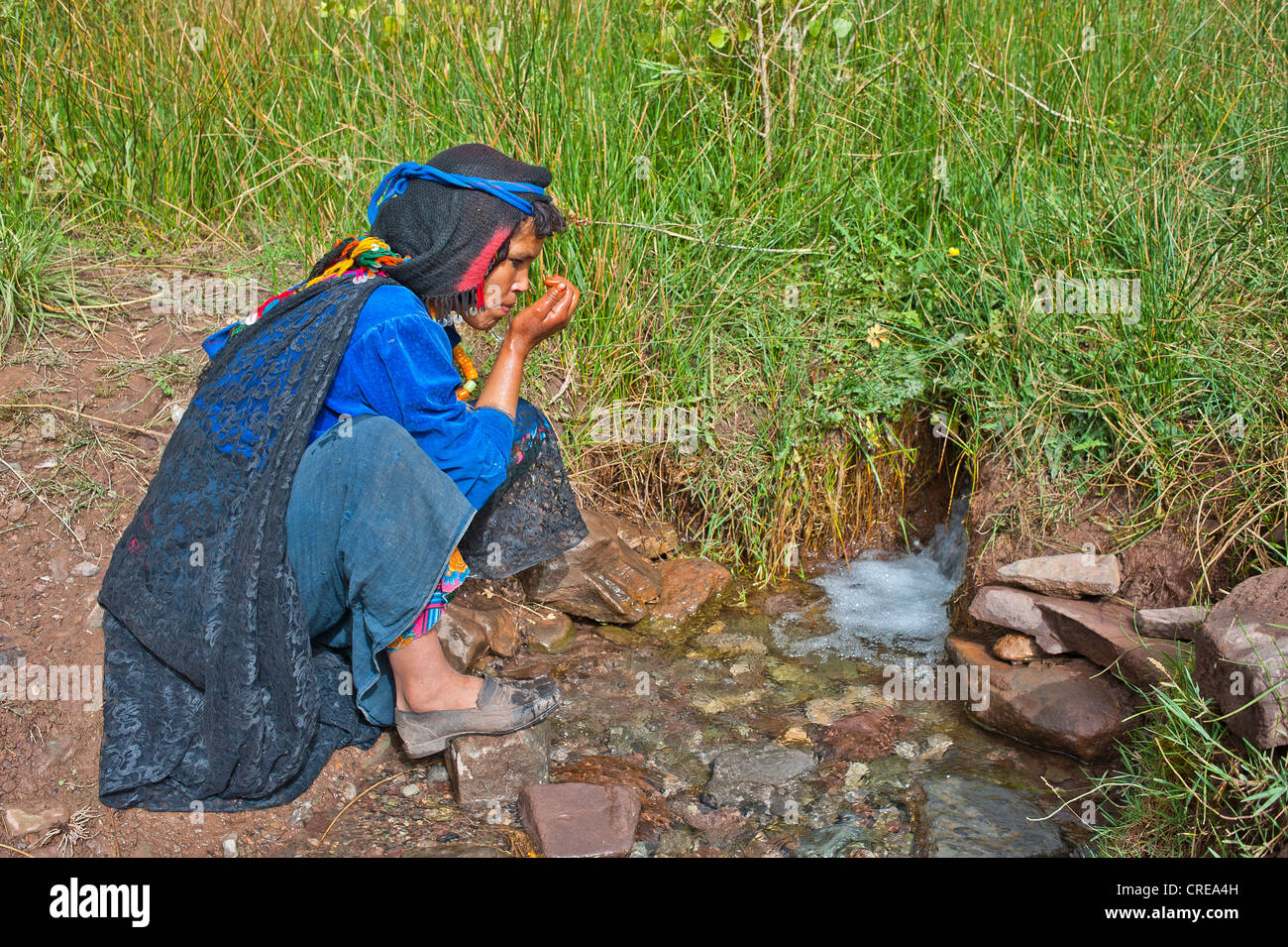 A Berber woman wearing a headscarf drinking water from a spring with