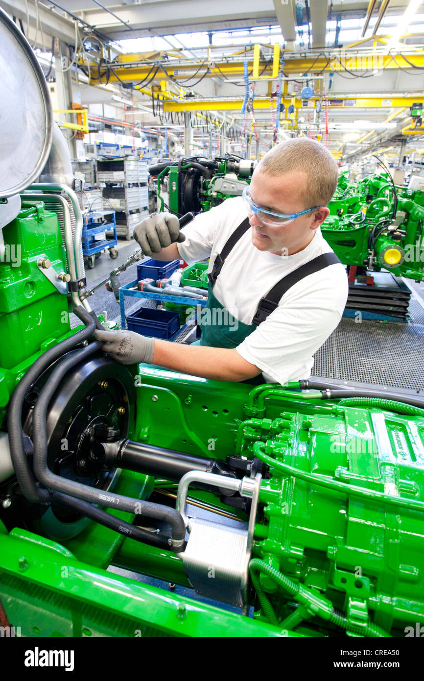 Worker is connecting hoses between the engine and the gearbox in the engine assembly area of the tractor production section at Stock Photo