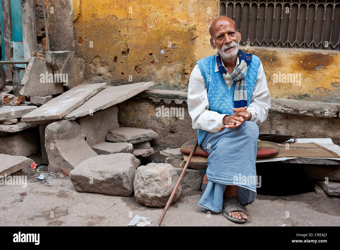 Elderly Indian man, Rajasthani, sitting on a stone bench with cushions in front of a house, resting, Bundi, Rajasthan, India Stock Photo