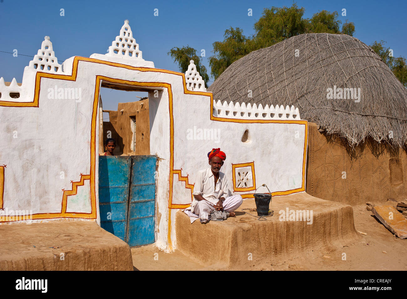 Rajasthani, Indian man wearing a dhoti and turban, sitting in front of his traditionally built and painted front door Stock Photo