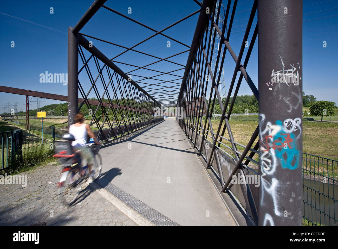 cyclist with a child driving over the bridge of the Emscher River at the Nordstern Park, Germany, North Rhine-Westphalia, Ruhr Area, Gelsenkirchen Stock Photo