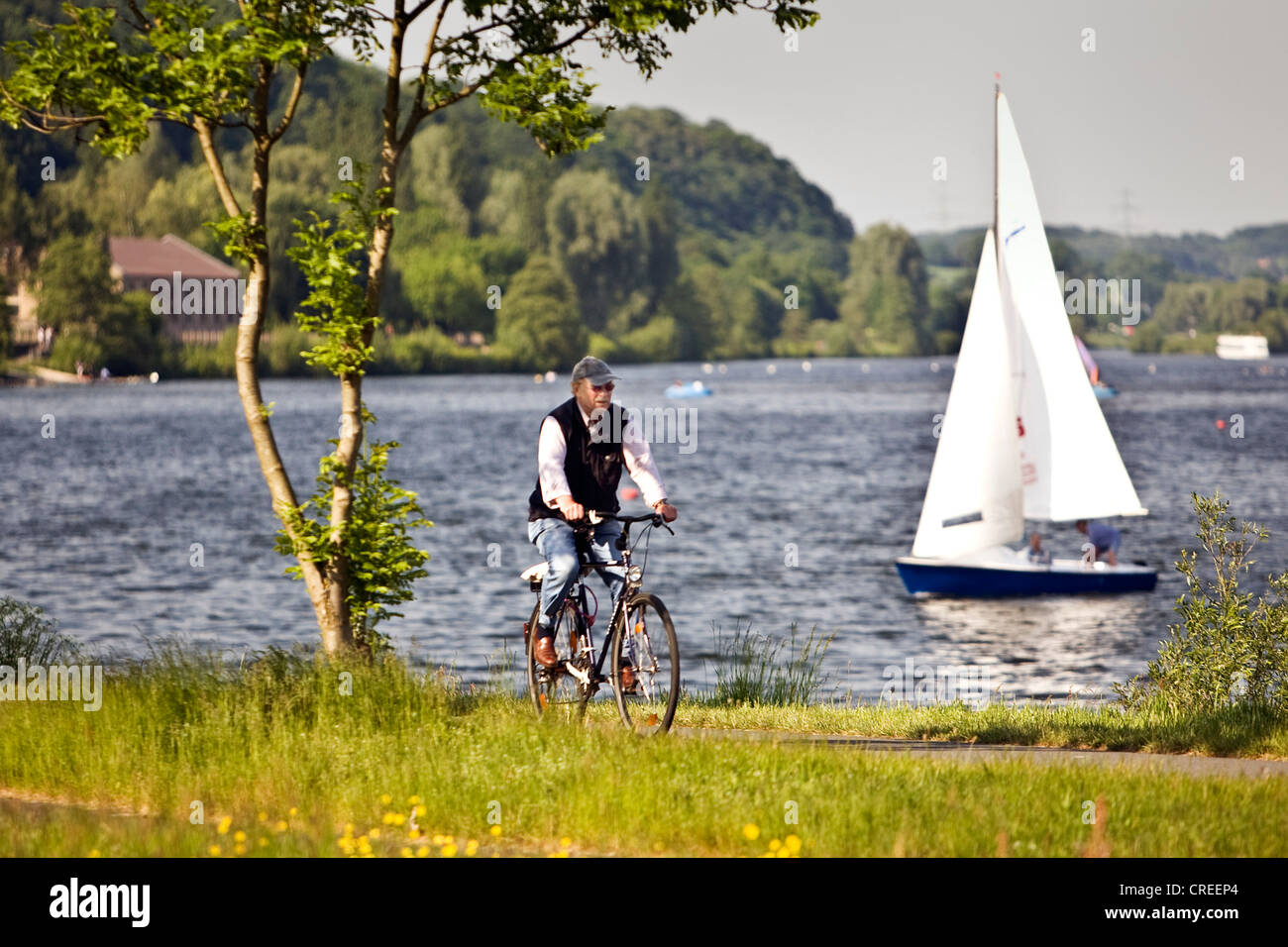 man on a bike at the Kemnader Stausee with sailing boat, Germany, North Rhine-Westphalia, Ruhr Area, Witten Stock Photo