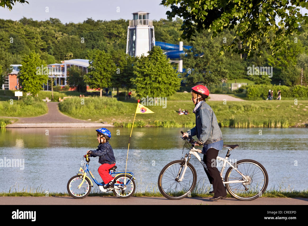 mother and child on bikes at the Kemnader Stausee with sailing boat, Germany, North Rhine-Westphalia, Ruhr Area, Witten Stock Photo