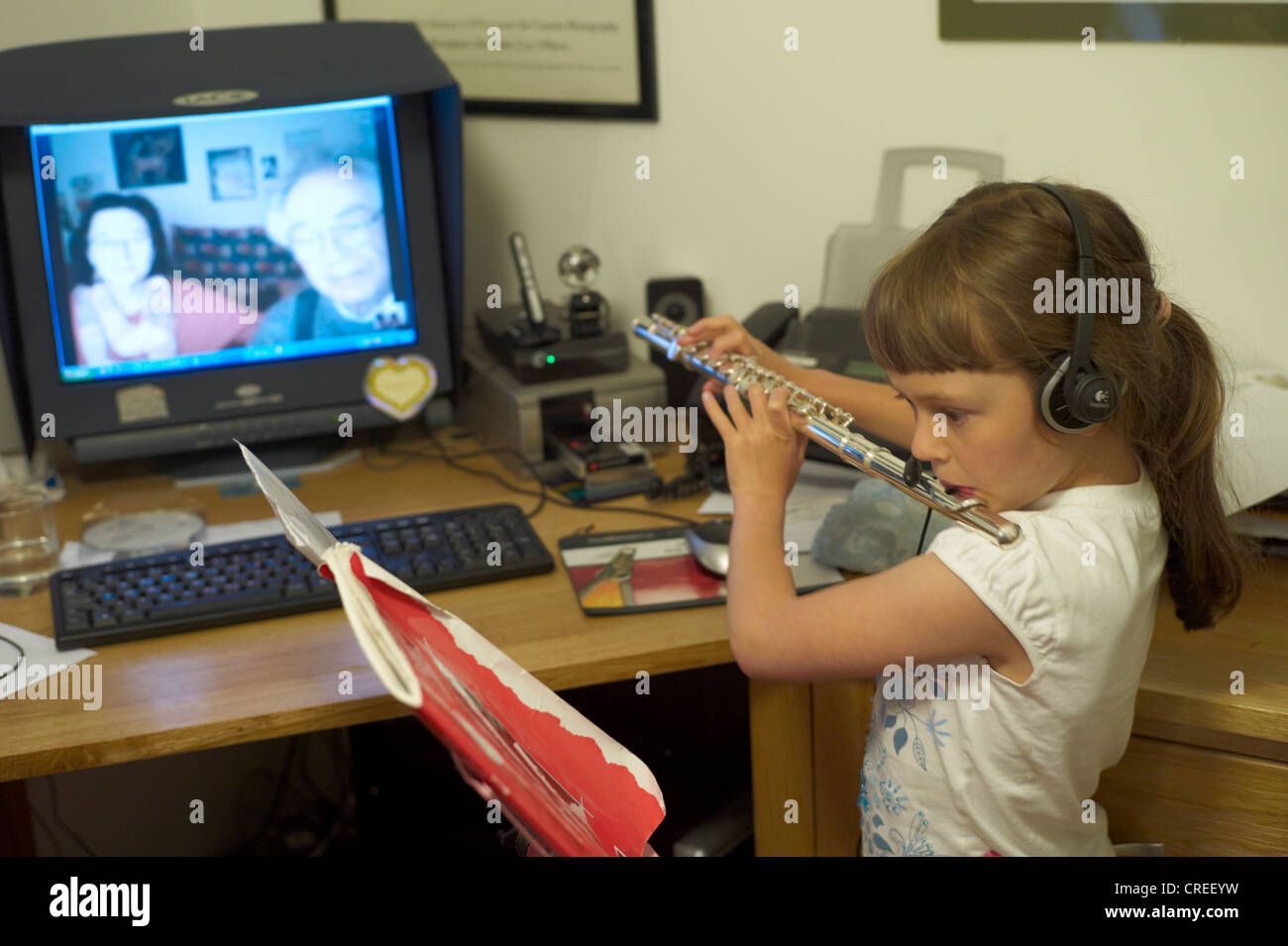 Child playing her flute to her grandparents via Skype Stock Photo