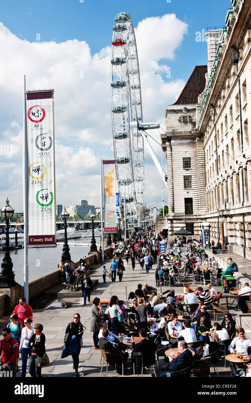 Tourists gather outside County Hall eating and drinking near the London Eye in London on a warm summers day Stock Photo
