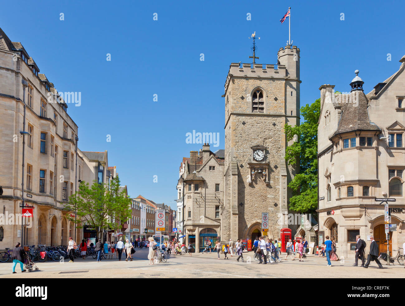 Shoppers in Oxford city centre with Carfax tower at Junction of High street Queen street St Aldates and Cornmarket street UK GB UK Europe Stock Photo