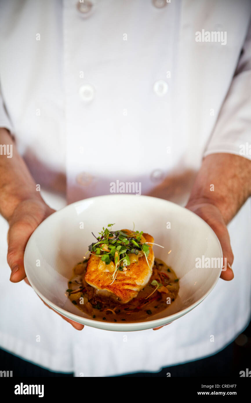 A chef holds a bowl of flounder. root vegetable cake, almonds, golden raisins & curry beurre
