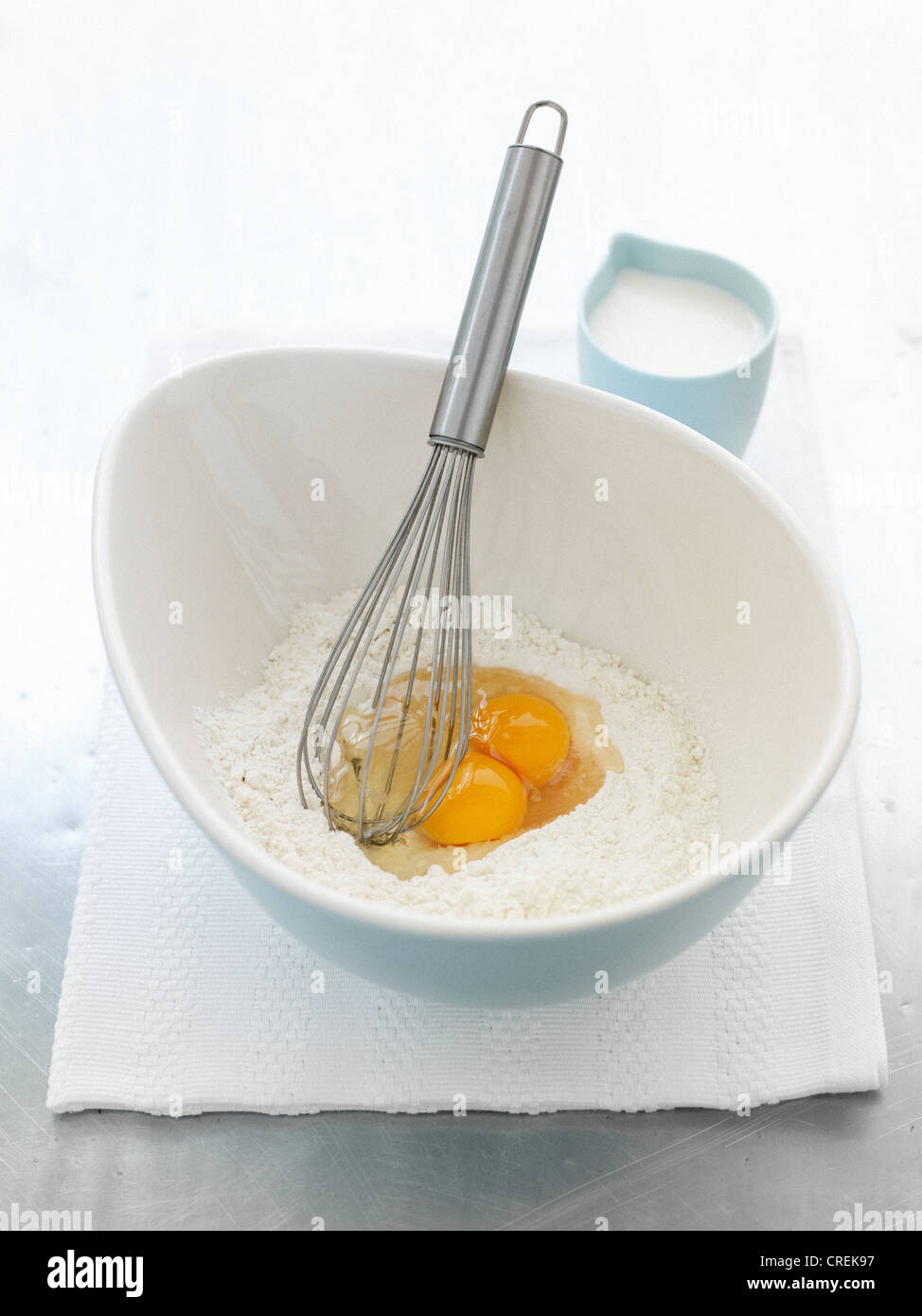Whisk in bowl with eggs and flour Stock Photo