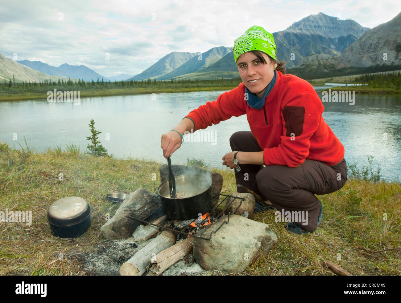 Young woman cooking on a camp fire, steering in a steaming pot, camping