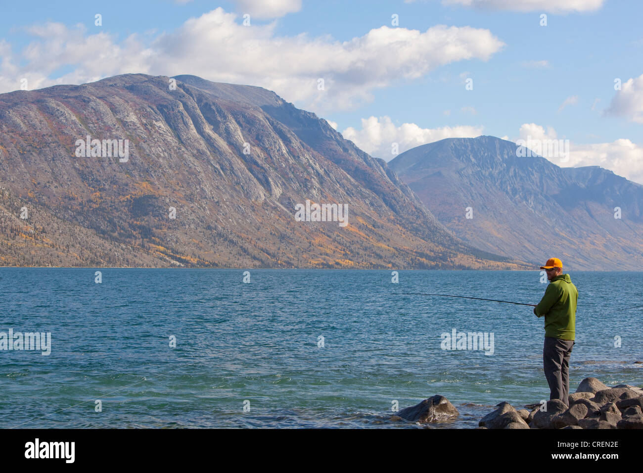 Man spin fishing, Kusawa Lake, mountains behind, Indian summer, autumn, Yukon Territory, Canada Stock Photo