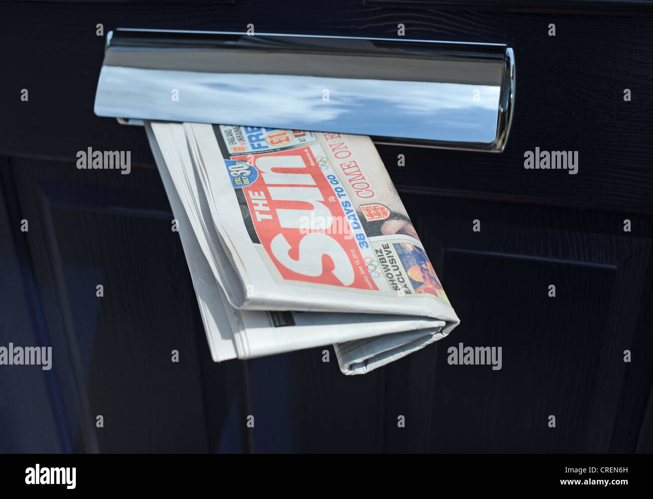 The Sun national newspaper owned by News International being delivered to a home with dark blue door and letterbox UK Stock Photo