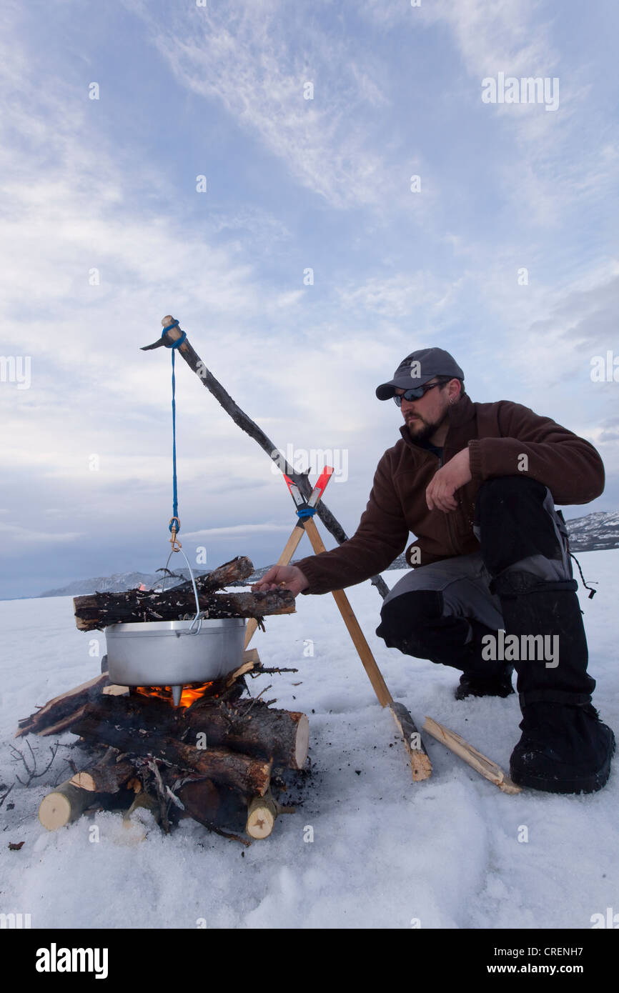 https://c8.alamy.com/comp/CRENH7/man-cooking-on-a-camp-fire-in-a-hanging-dutch-oven-ice-of-frozen-lake-CRENH7.jpg