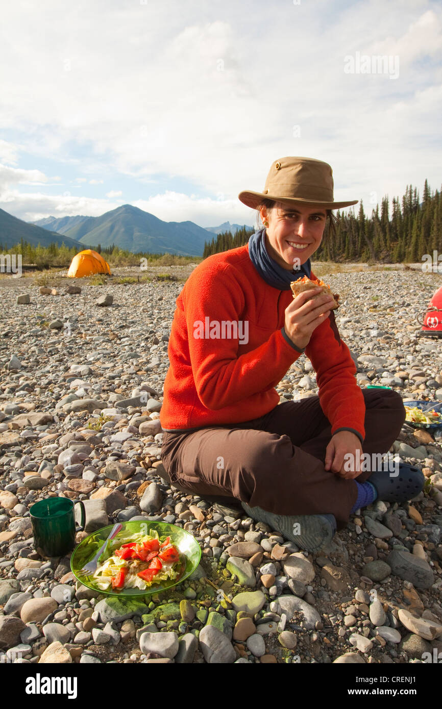Young woman enjoying a hamburger, tent behind, camping, Wind River, Yukon Territory, Canada Stock Photo