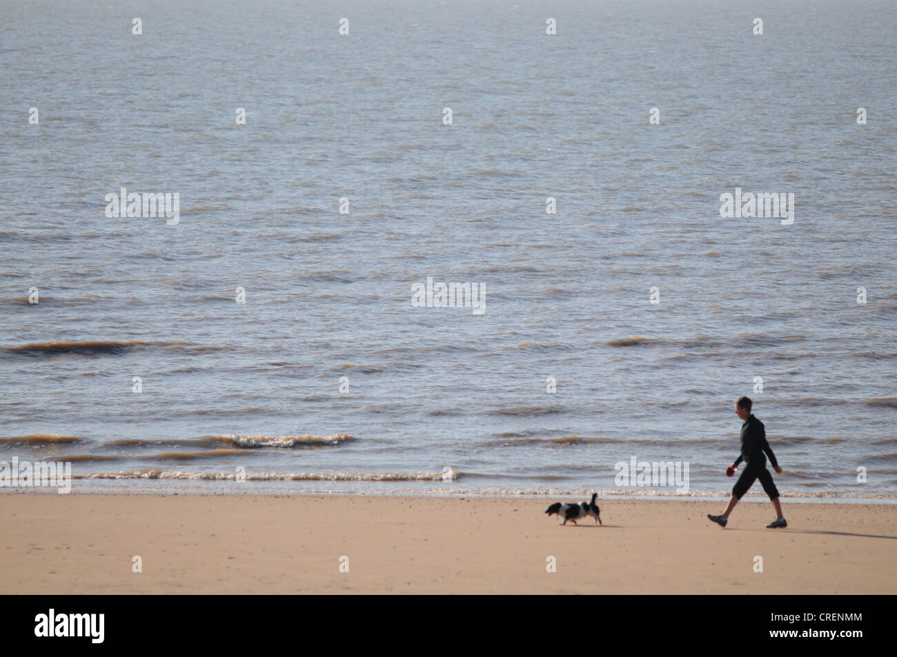 A woman walks her dog in the early morning along the beach at Frinton in Essex Stock Photo