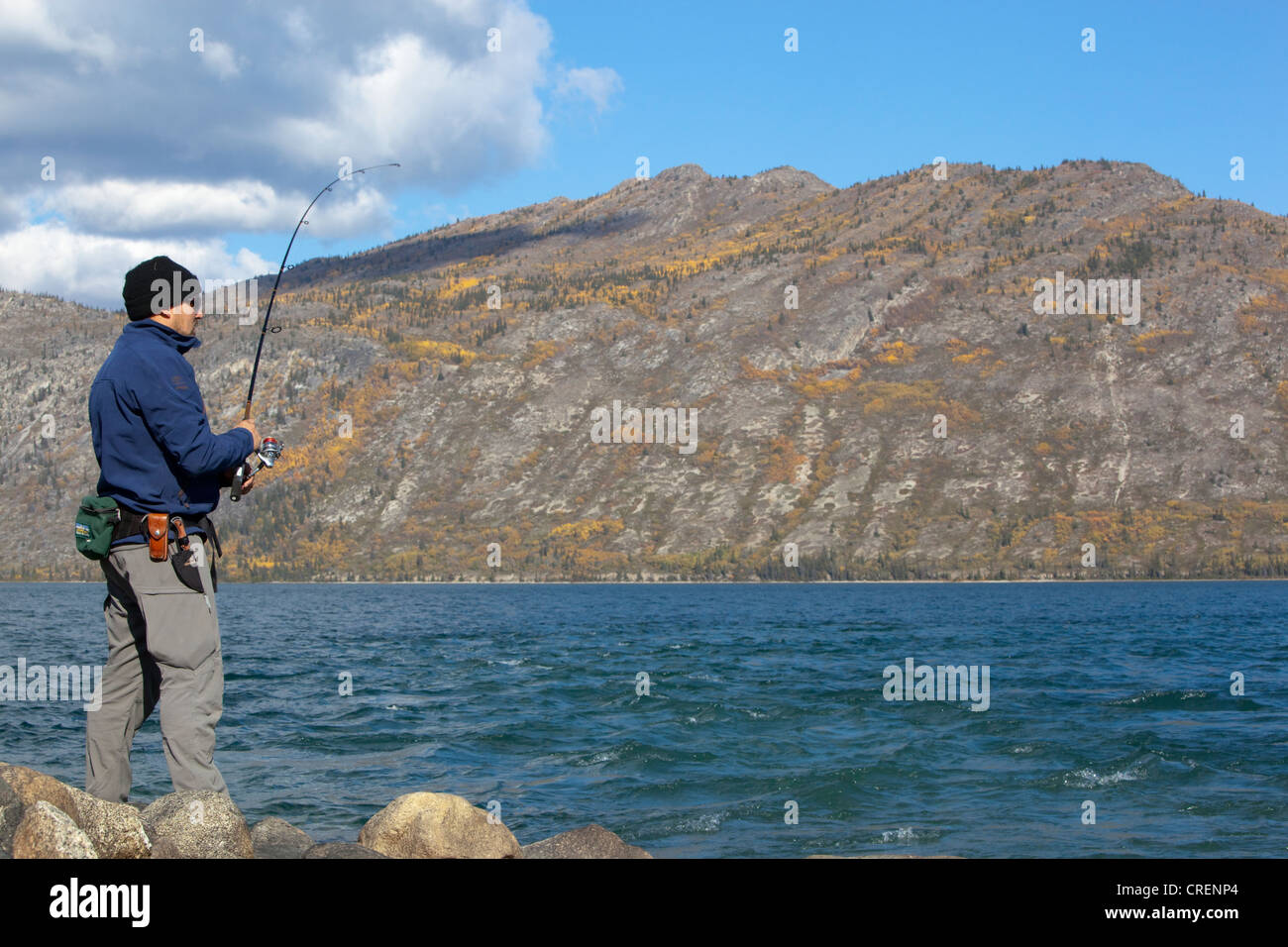 Man spin fishing, fighting a fish, Kusawa Lake, mountains behind