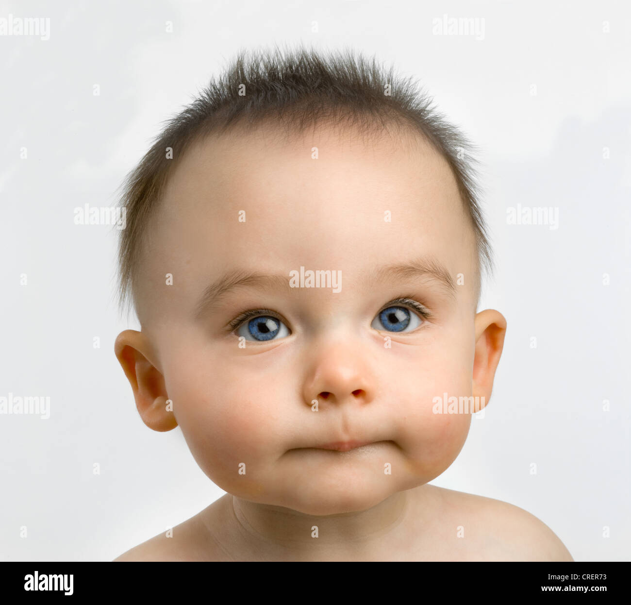 Head and shoulders of a captivating 8 month old baby with spiky hair looking  straight ahead with a great expression Stock Photo