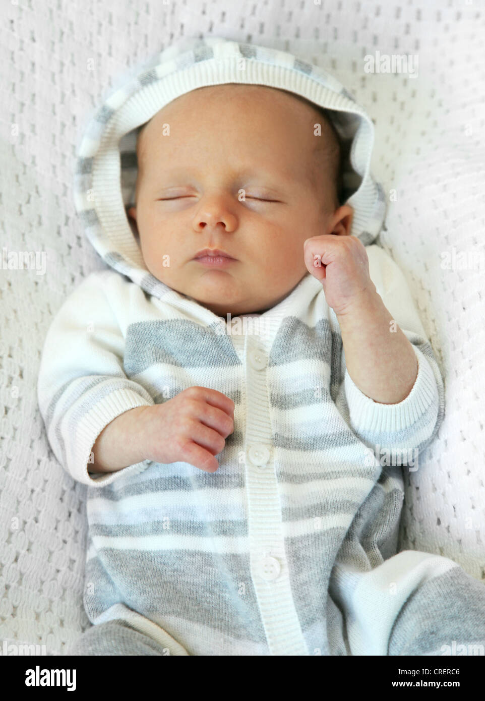 5 week old baby sleeping on its back in a striped hooded outfit Stock Photo