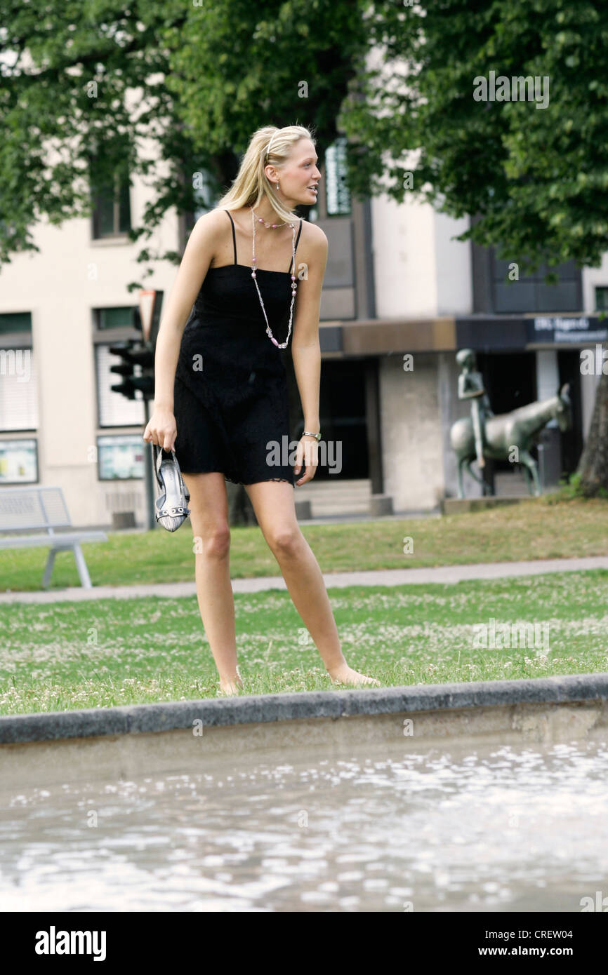 young blond woman wearing black summer dress standing near fountain, Germany Stock Photo