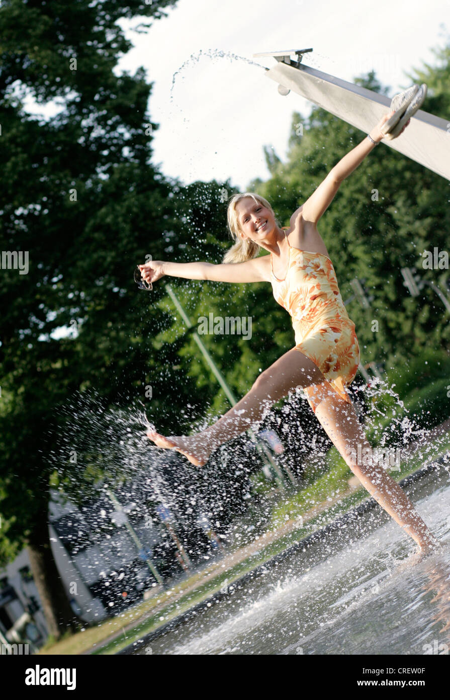young blond woman in summer dress splashing with water of a fountain, Germany Stock Photo