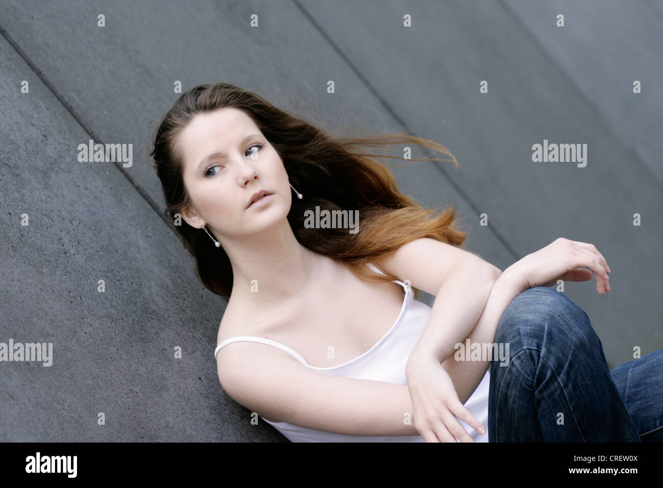 young beautiful woman crauching beside a wall, Germany Stock Photo