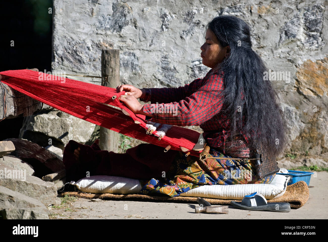 A tribal woman uses a BACKSTRAP LOOM to make red cloth in GYASUMDO VILLAGE near Manang on the ANNAPURNA CIRCUIT, Nepal, Kathmandu Stock Photo
