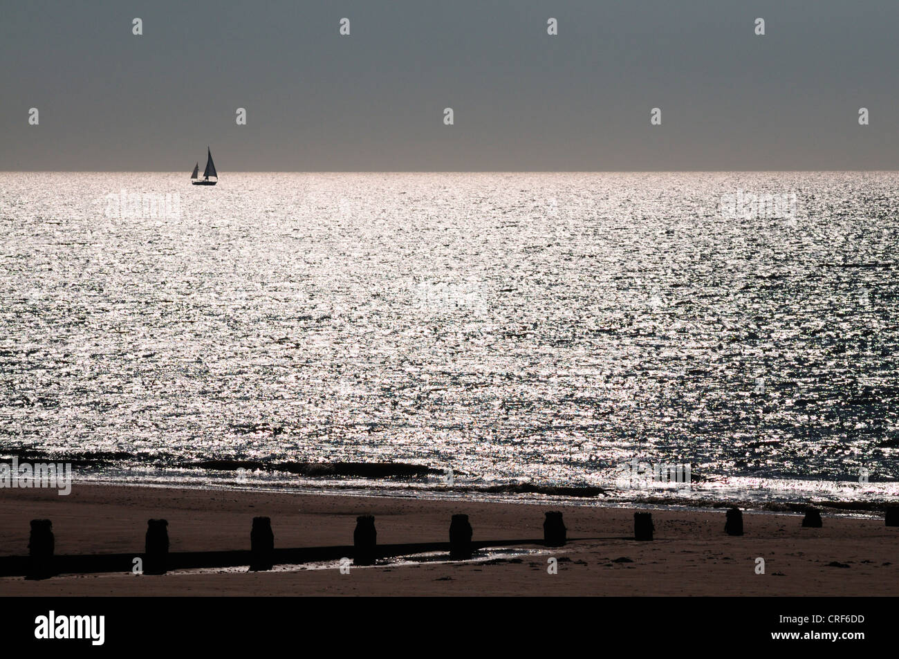 Silhouetted sailing boat on the horizon in bright reflected early morning light Stock Photo