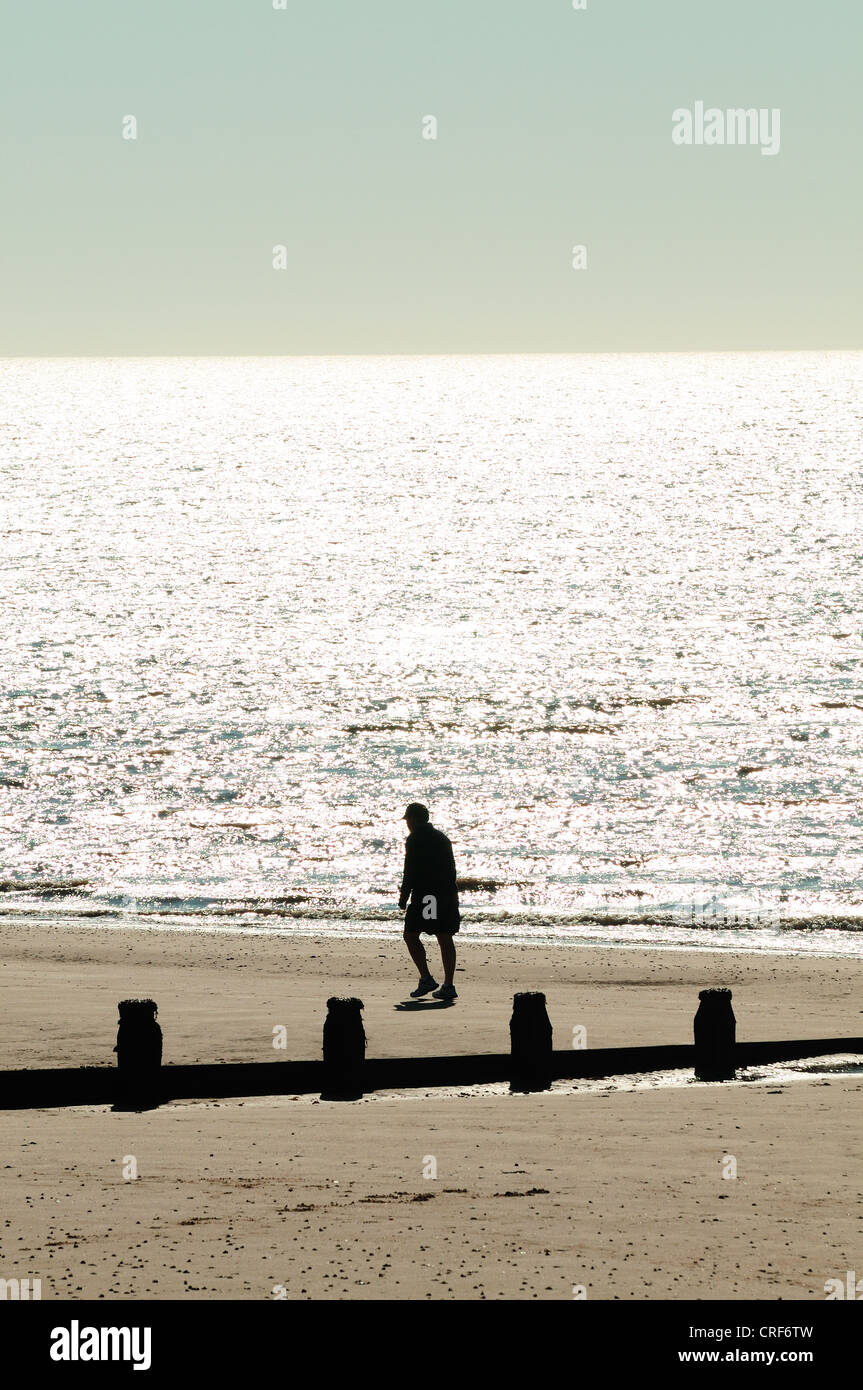 A man walks along the edge of the sea on a beach in the early morning, Frinton Essex Stock Photo