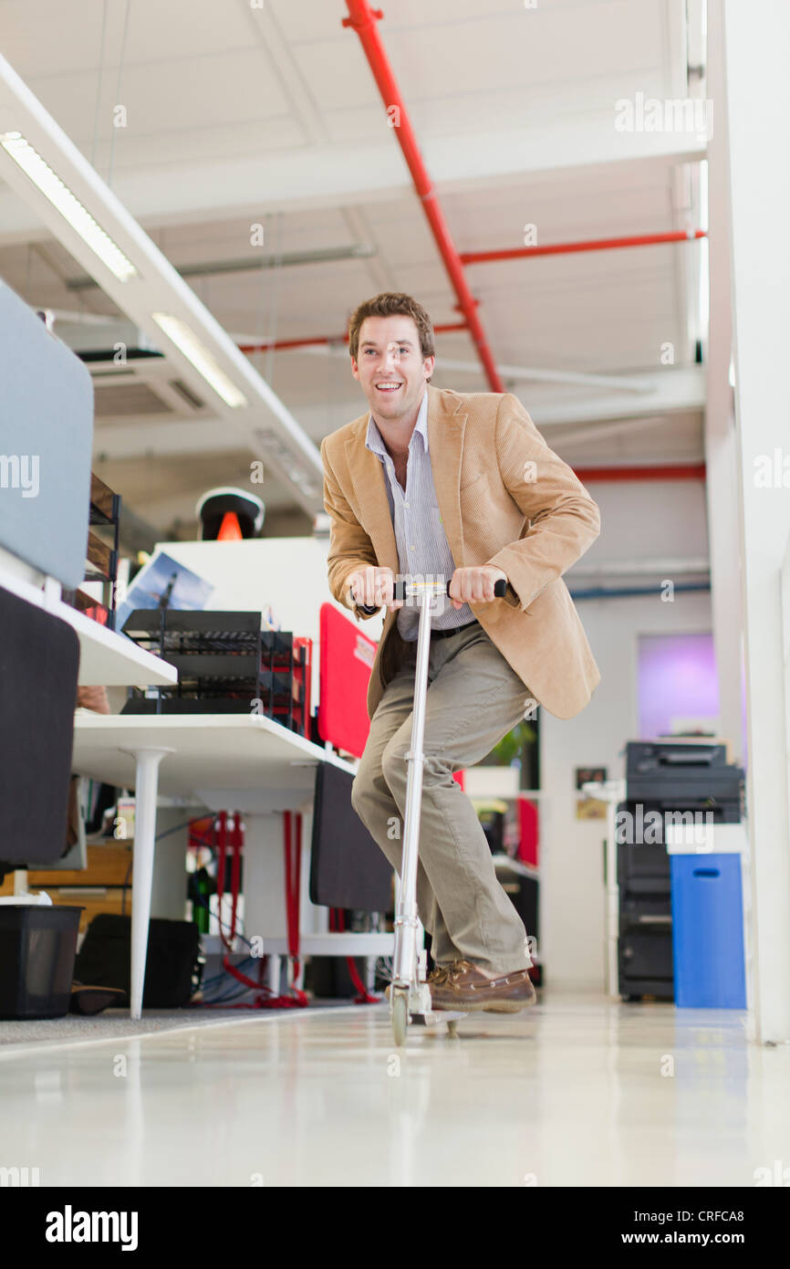 Businessman riding scooter in office Stock Photo Alamy