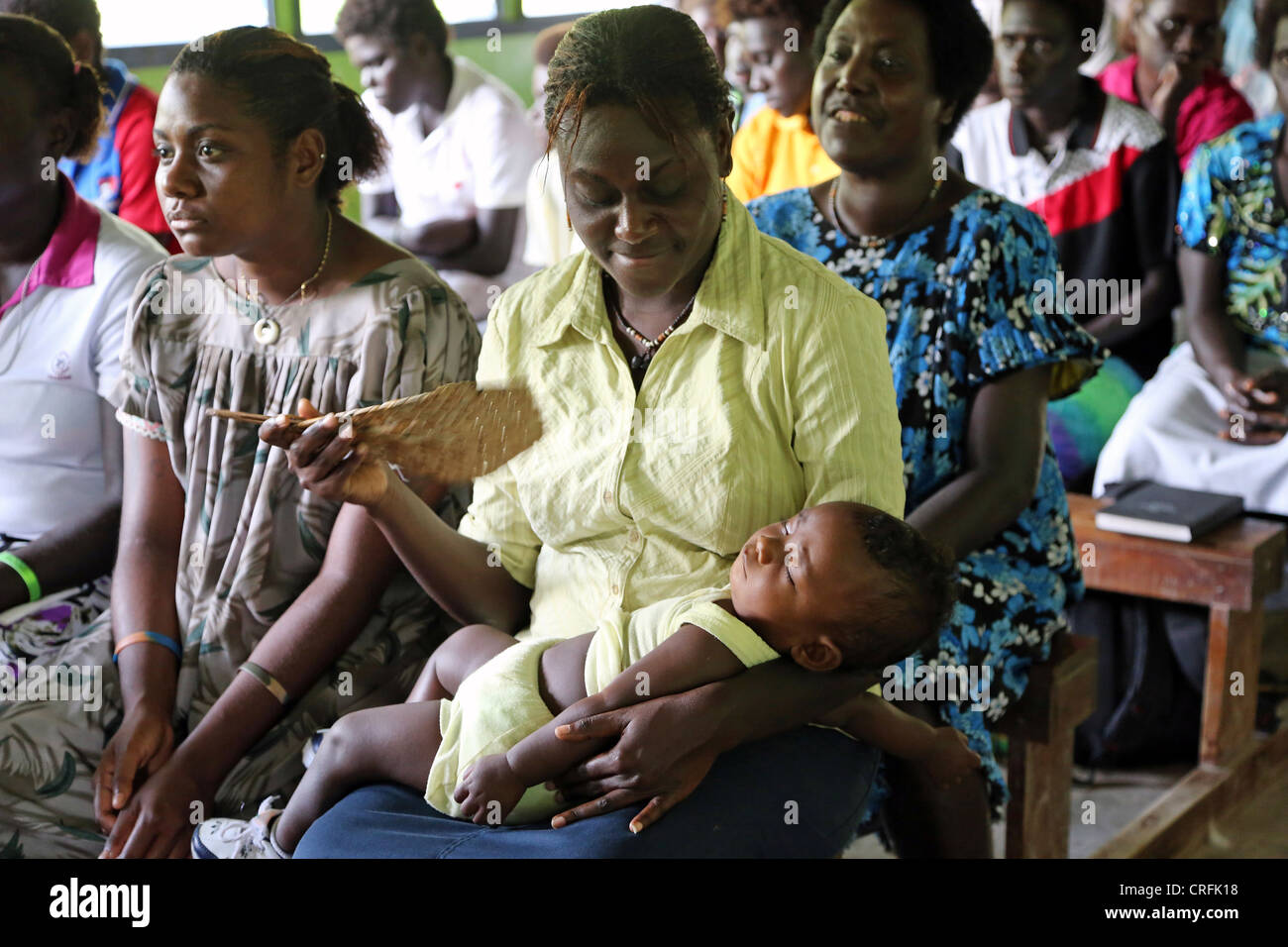 Mother fans out cool air to her sleeping baby in a church on Bougainville Island, Papua New Guinea Stock Photo