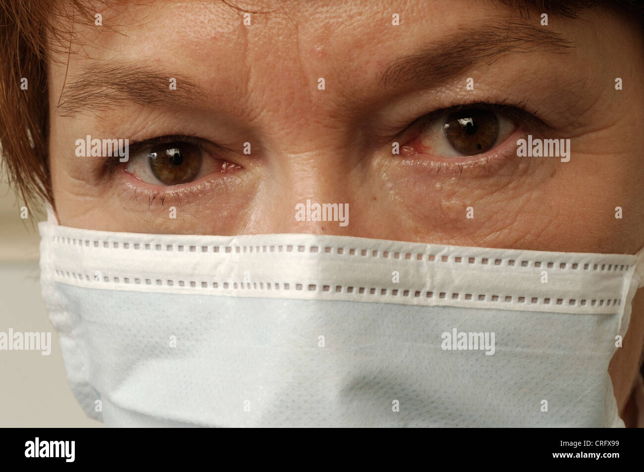 Facial close up of a mature woman with staring eyes wearing a surgical mask. Stock Photo