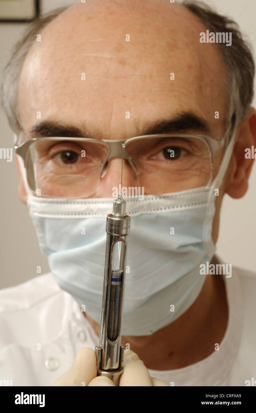 Facial close up of a dentist wearing protective glasses and a surgical mask testing a syringe. Stock Photo