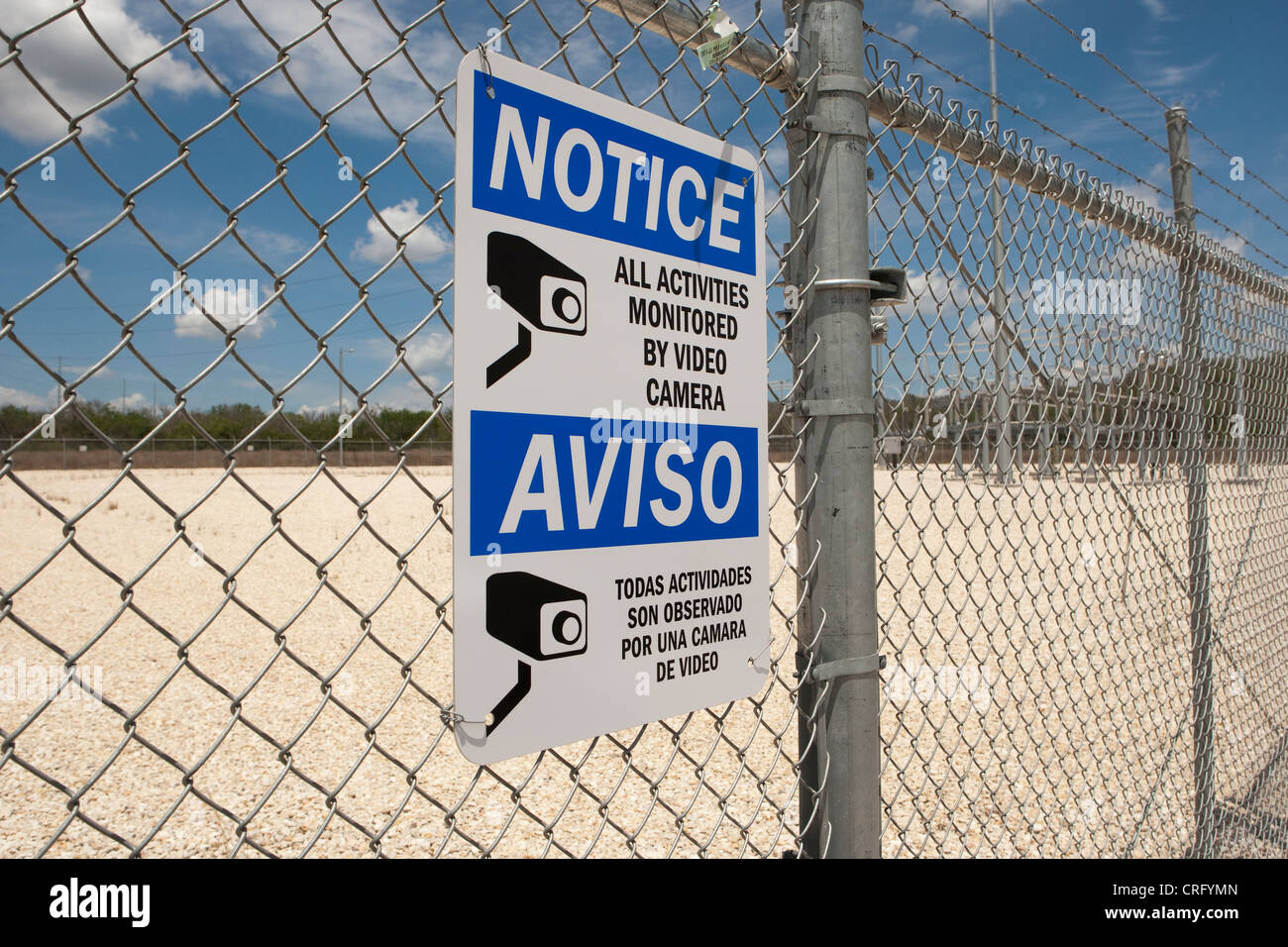 Bilingual sign in English and Spanish posted on chain link fence reads