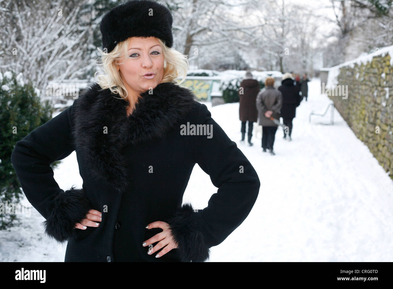 blond woman wearing black fur coat and fur cap standing in snow Stock Photo