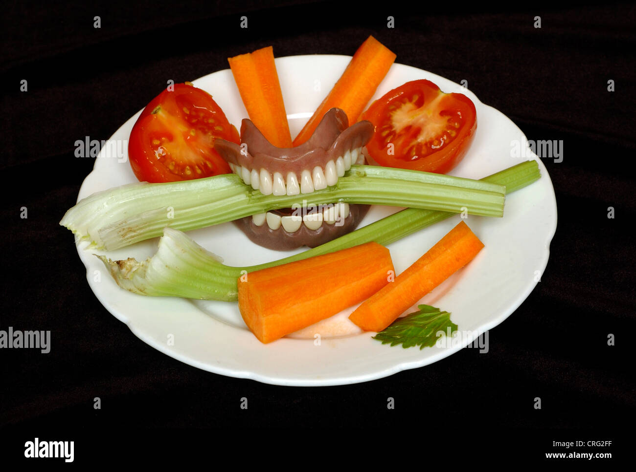 A stick of celery in between the teeth of a set of dentures, on a plate