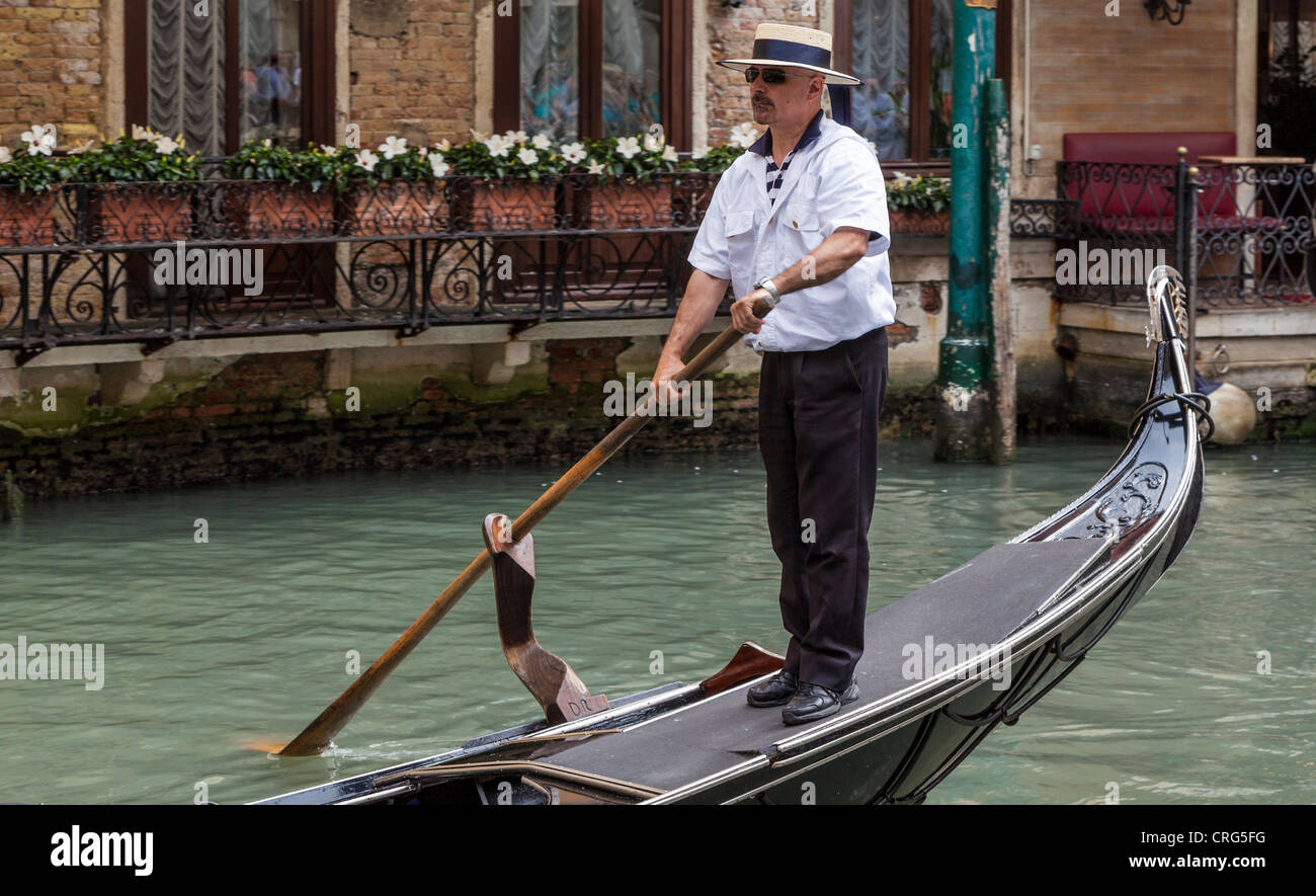 A gondolier wearing a hat and standing on the back of his gondola. Stock Photo